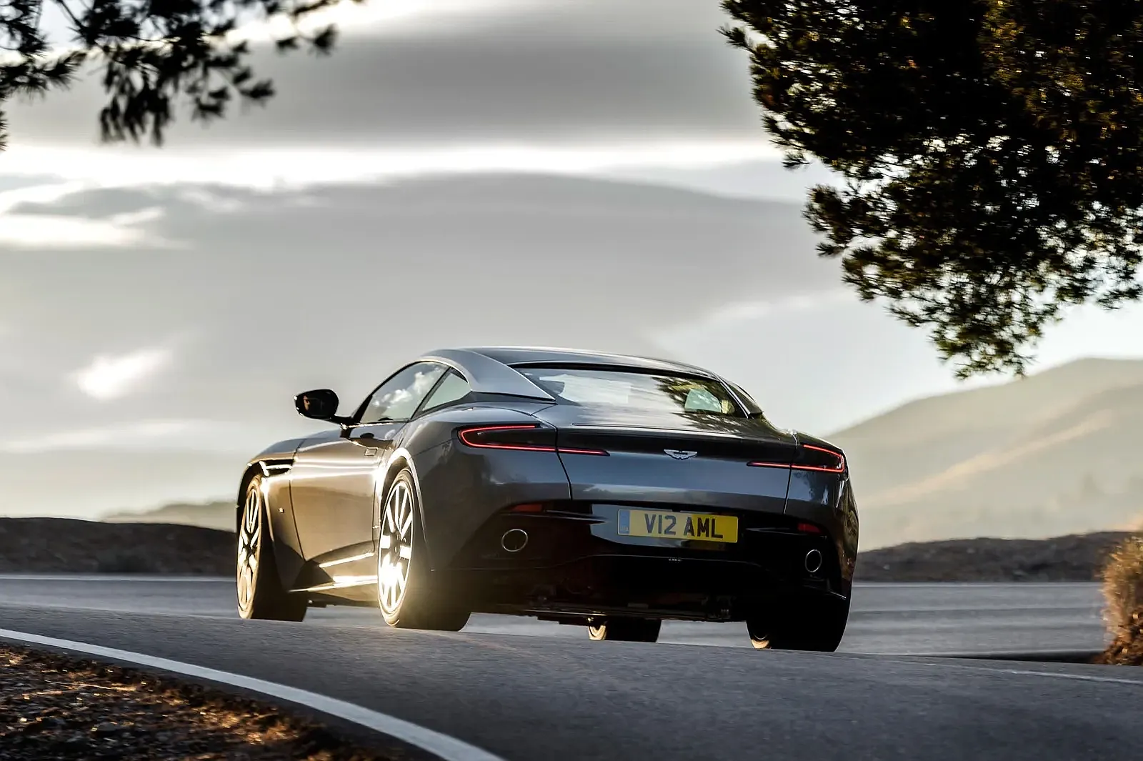 Grey Aston Martin DB11 leaving a corner at sunset