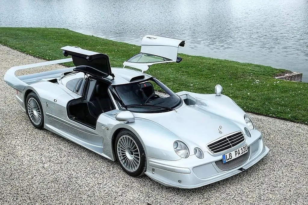 Silver Mercedes-Benz CLK GTR with its doors open beside a lake