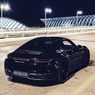 Black Porsche 911 (992) at night in front of a modern bridge