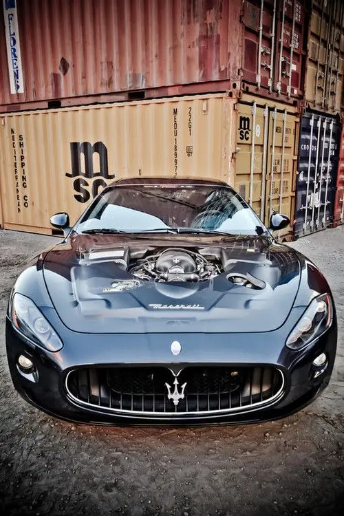 Maserati GranTurismo with an open bonnet in front of shipping containers