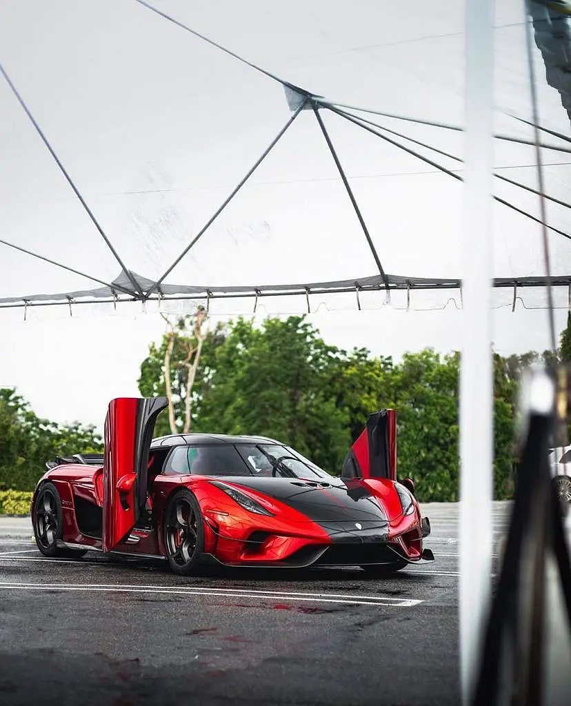 Red hypercar with its doors raised under a tent