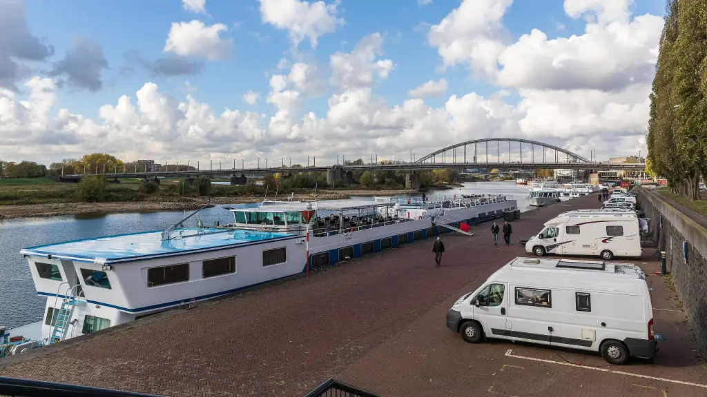 Two white motorhomes parked beside a river with a steel arch bridge in the background